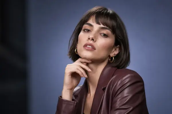 Beauty & Fashion Fotos 5 Hochwertiges Beauty-Porträt von PM STUDIOS München: Eine Frau mit braunem Kurzhaarschnitt und bordeauxroter Lederjacke posiert mit der Hand am Kinn vor einem edlen graublauen Hintergrund.