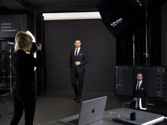 Businessfotos 2 Blick hinter die Kulissen bei PM STUDIOS München: Eine Fotografin fotografiert einen Geschäftsmann im Anzug in einem modernen Fotostudio mit Profoto-Equipment.