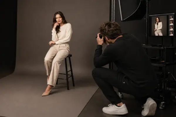 Gutscheine 3 Professionelles Einzel-Porträtshooting bei PM STUDIOS München: Ein Fotograf in Aktion fotografiert ein sitzendes Modell vor grauem Hintergrund; Live-Bildübertragung (Tethered Shooting) auf einen Studiorechner zur sofortigen Auswahl.