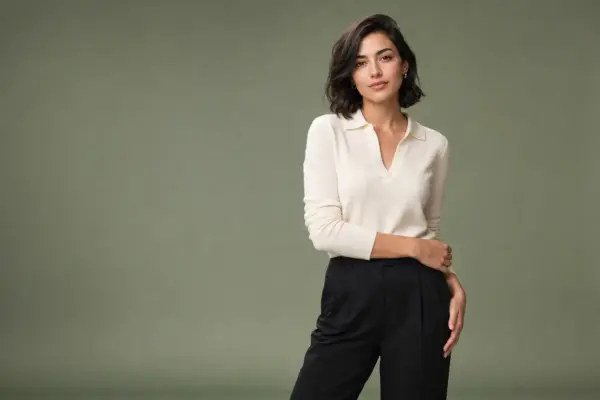 Comp card shooting 2 Professional lifestyle portrait for a model portfolio by PM STUDIOS Munich: Woman posing in a cream polo sweater and black trousers against a muted olive-green studio background.